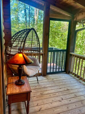 A wooden deck with a hanging chair and a table with a lamp. - Licklog Lodge (Ellijay)