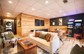 A modern living room with a sofa, armchairs, a coffee table, and a pool table. There are gaming machines and a small dining area. - Licklog Lodge (Ellijay)