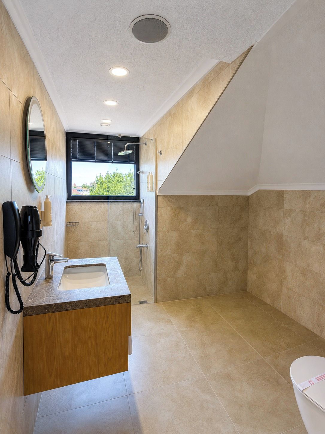 Un baño moderno con tocador de madera, un espejo grande, ducha y un inodoro.