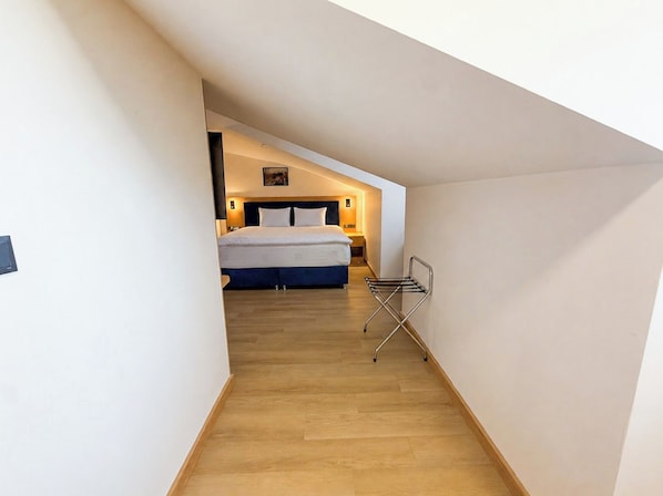 Un pasillo estrecho que conduce a un dormitorio con cama, mesita de noche y lámpara de pared.