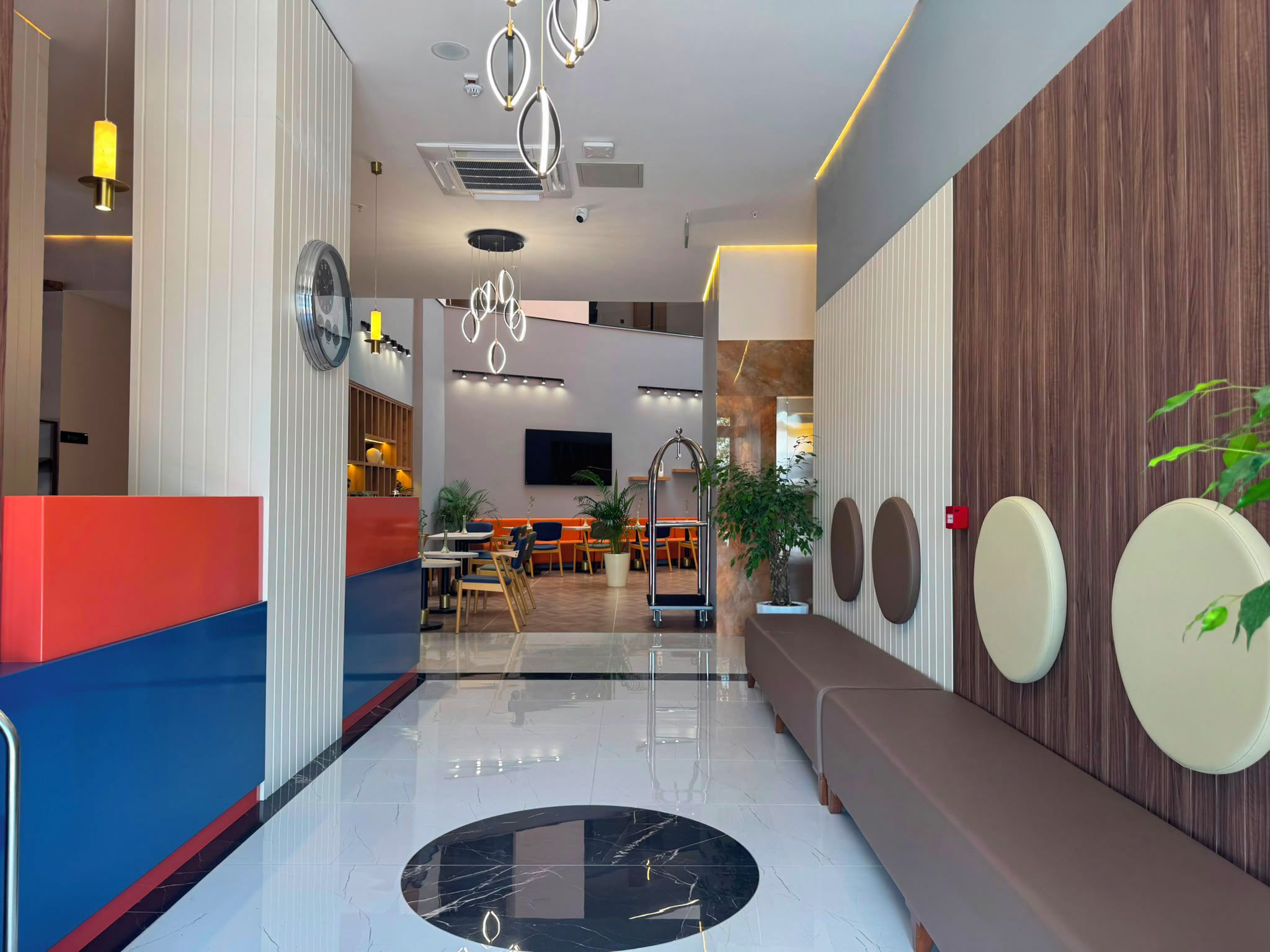 A modern hotel lobby with a reception desk, seating area, and a dining section.