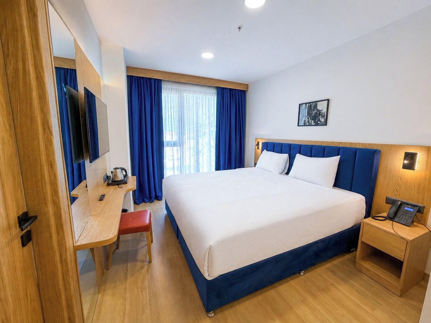 A hotel room with a bed, bedside table, desk, chair, and a television.