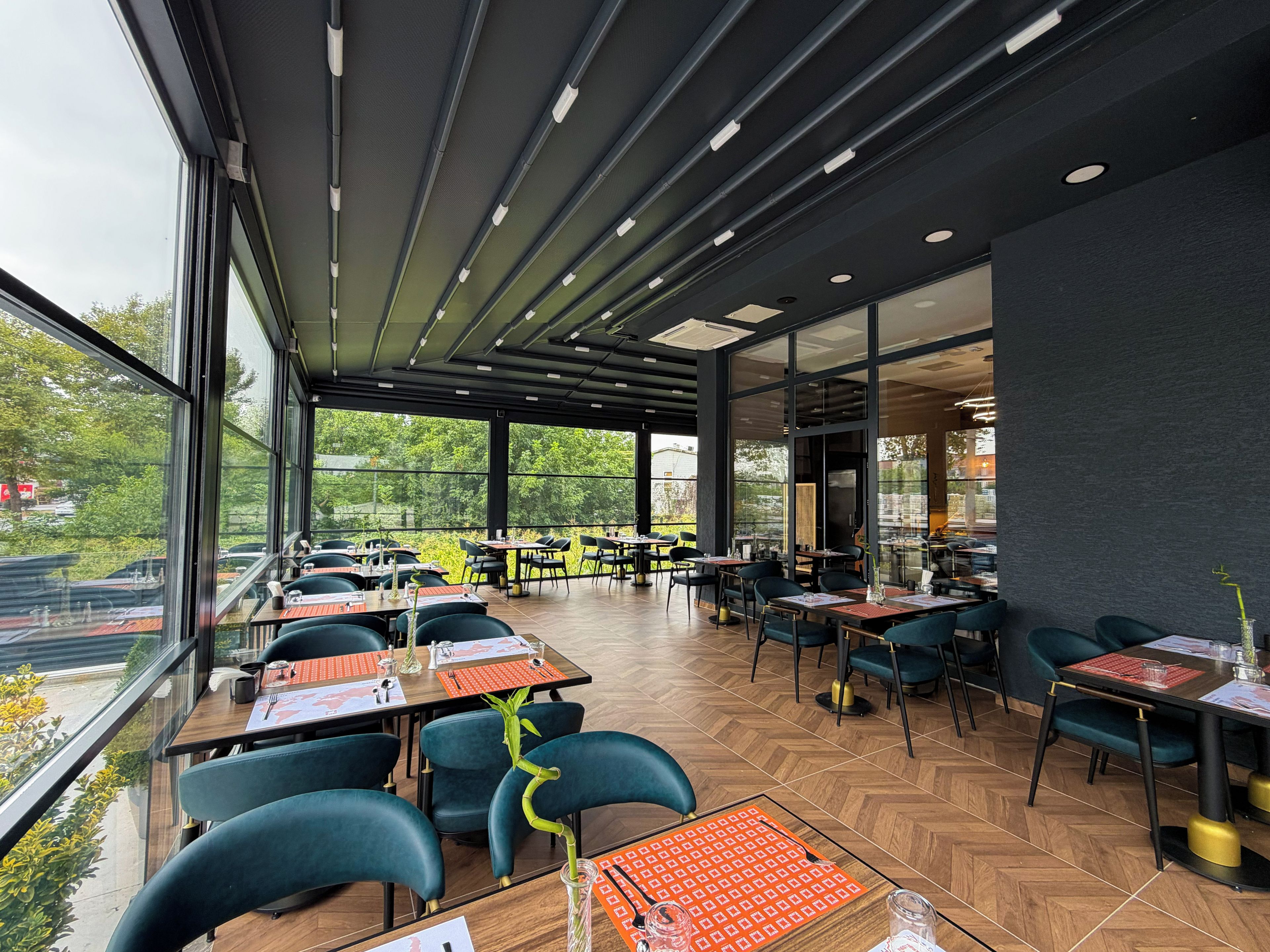 Un restaurante moderno con amplios ventanales, suelo de madera y sillas negras.