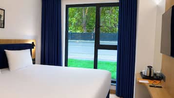 Une chambre d’hôtel avec un lit, un bureau doté d’une bouilloire et une vue sur la verdure environnante.