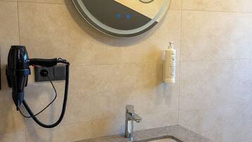 Un baño con un espejo redondo, un lavabo, un secador de pelo y una botella de loción.