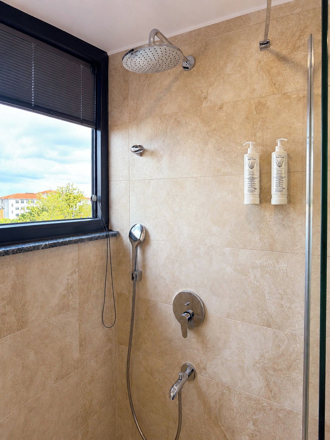 Un baño moderno con cabina de ducha de vidrio, ducha de mano, grifo empotrado en la pared y dos botellas de champú.