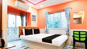 Een hotelkamer met een bed, een stoel, een raam met gordijnen, een wandairconditioner en een ingelijst schilderij.