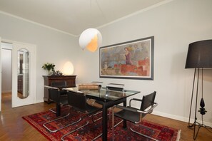 Ein Essbereich mit einem Glastisch, schwarzen Stühlen, einem rot gemusterten Teppich, einem Bild an der Wand und einer Lampe.