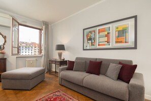 Ein Wohnzimmer mit grauem Sofa, passendem Hocker, Stehlampe und abstrakter Kunst an der Wand.