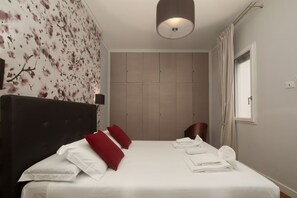 Ein Hotelzimmer mit Bett, Kopfteil, Wand mit Blumenmuster, Fenster mit Vorhängen und einer Deckenleuchte.