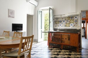A kitchen with a tiled backsplash, a wooden table with chairs, a television, and a window with a view of greenery. - Ariosto Aparment by San Frediano&Smn (Florence)