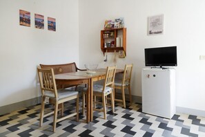 Ein Essbereich mit Holztisch und -stühlen, einem kleinen Kühlschrank und einem Fernseher auf einem Standfuß.