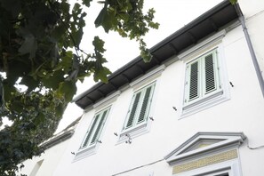 Ein Gebäude mit drei Fenstern, jeweils mit Fensterläden, und einem dekorativen Gesims.