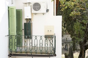 Ein Balkon mit Metallgeländer, eine weiße Wand mit Klimaanlage und eine grüne Tür.