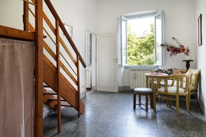 A room with a wooden staircase, a window with a view of greenery, and a table with chairs. - Ariosto Aparment by San Frediano&Smn (Florence)