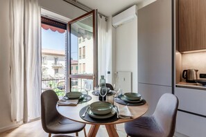 A dining area with a table set for two, a view of the outside, and a kitchen area with cabinets and appliances. - Otium Lake Como by MyHomeInComo (Como)