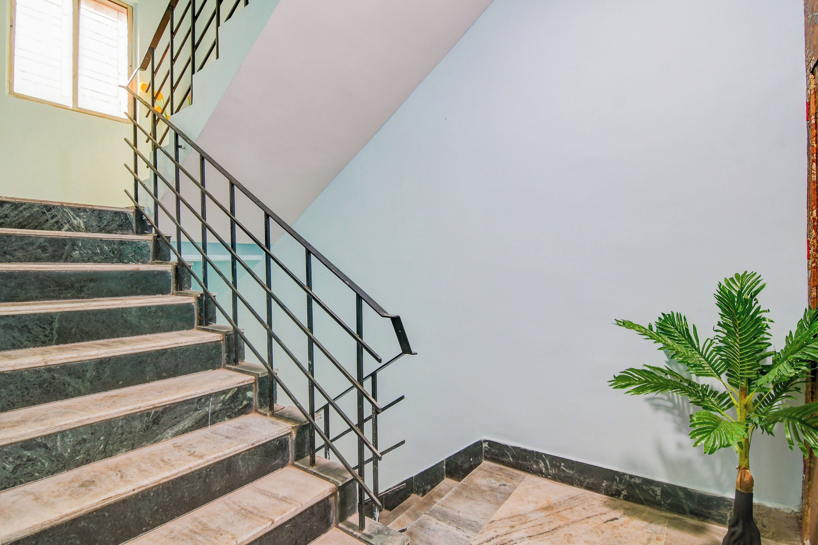 Una escalera con escalones de mármol y barandilla de metal, que lleva a una plataforma con una planta en maceta.