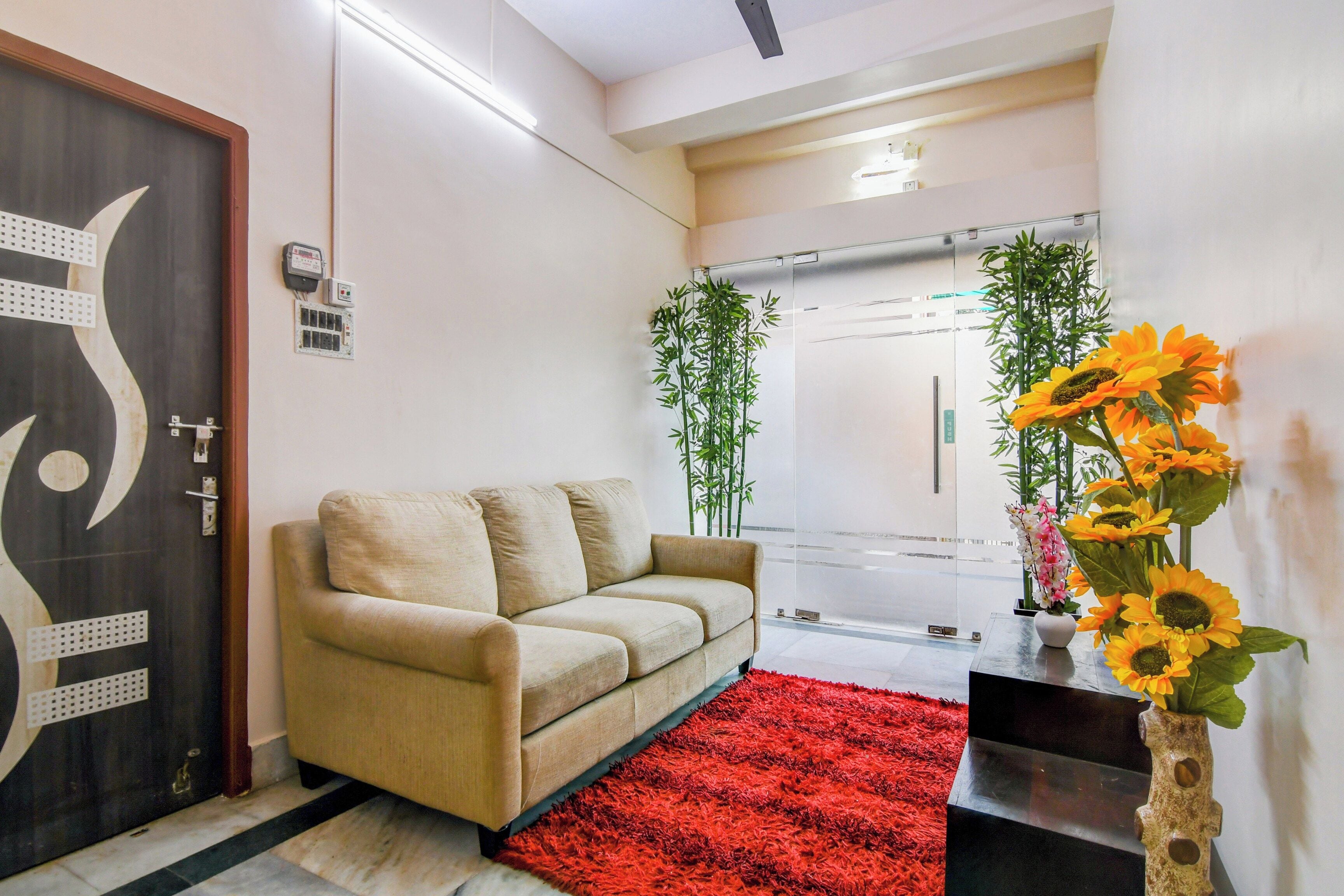 A modern hotel lobby with a beige sofa, a red rug, and a vase of sunflowers.