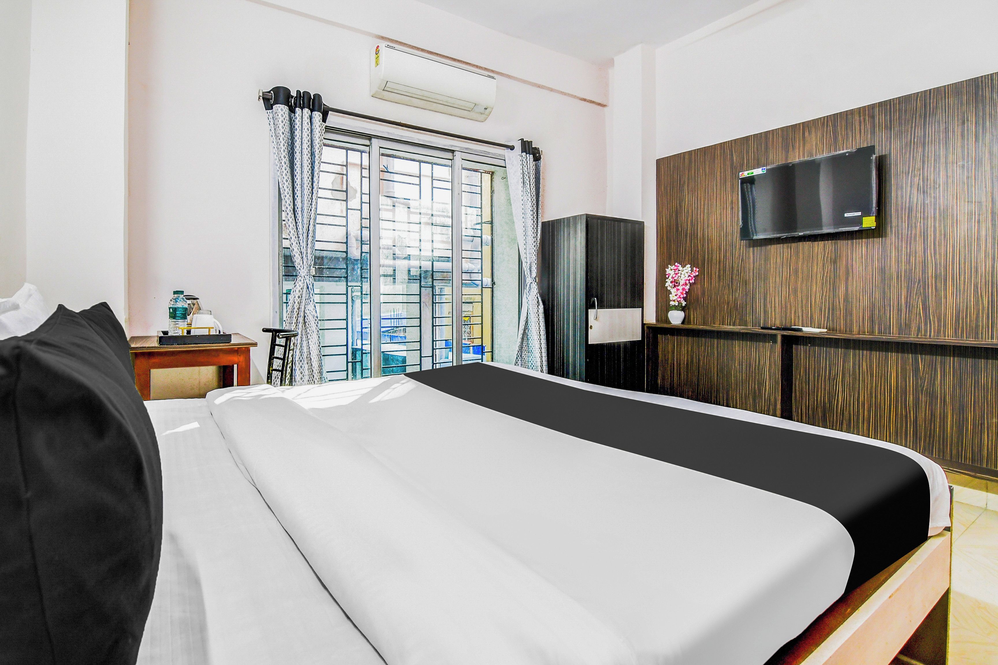 A hotel room with a bed, a desk with a chair, a television on the wall, and a window with curtains.
