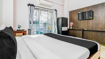 A hotel room with a bed, a desk with a chair, a television on the wall, and a window with curtains.