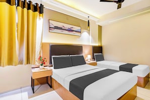 Hotellihuone, jossa on kaksi sänkyä, yöpöytä lampun kanssa, taulu seinällä ja ikkuna, jossa on verhot.