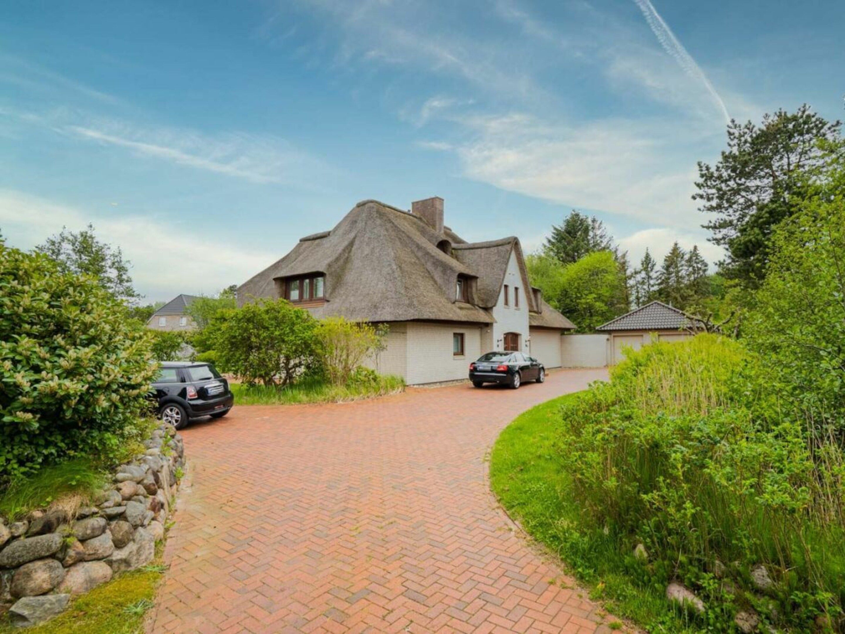 A house with a thatched roof, a paved driveway, and a stone wall on one side.