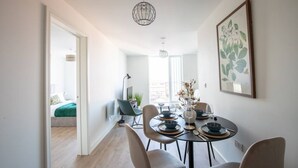 Un comedor con una mesa redonda, sillas y un florero con flores. Se ve una ventana con vistas al exterior.