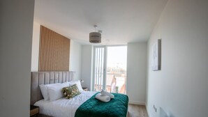 Un dormitorio moderno con cama, ventana con persianas, radiador y una lámpara fijada a la pared.