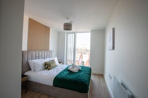 A modern bedroom with a bed, a window with blinds, a radiator, and a wall-mounted light fixture. - Sapphire Court Modern 2 Bedroom Flat 88 (Birmingham)