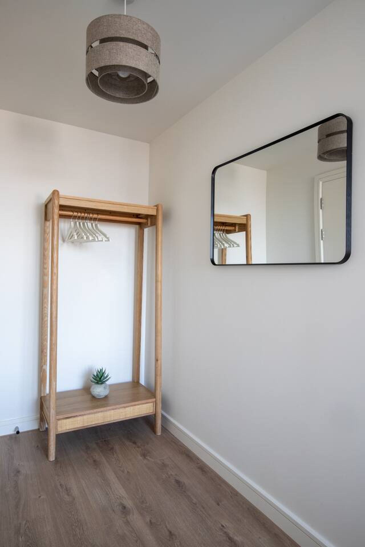 A room with a wooden bench, a hanging clothes rack, a small potted plant, and a wall-mounted mirror.