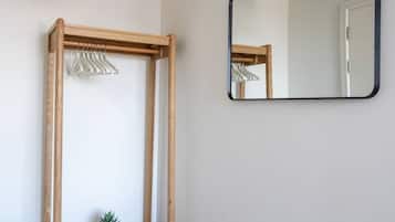 A room with a wooden bench, a hanging clothes rack, a small potted plant, and a wall-mounted mirror.