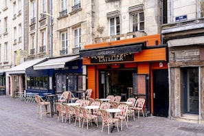 Een café met terras, een bord waarop 'L'ATELIER' staat, en een straatnaambordje met 'PLACE SAINT-SAUVEUR'.