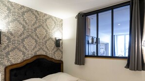 A hotel room with a bed, a window with curtains, and a patterned wallpaper. - The Charm of Place Saint-Sauveur (Caen)