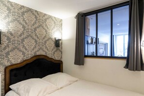Een hotelkamer met een bed, een raam met gordijnen en behangpapier met een patroon.