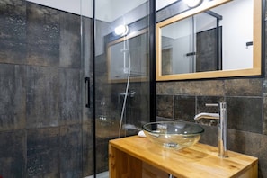 Een moderne badkamer met een douchecabine van glas, een houten wastafelmeubel en een grote spiegel.