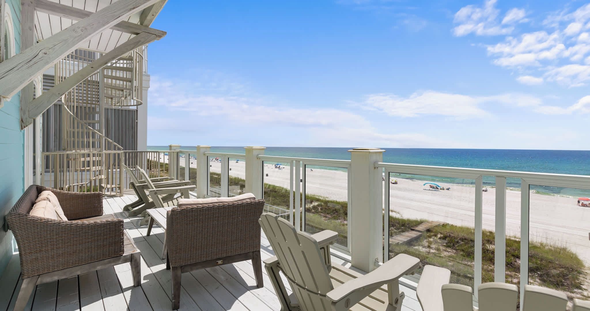 A wooden deck with wicker furniture overlooking a beach.
