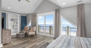 A bedroom with a large window, a bed, a chair, a small table, and a shelf with decorative items. - Ocean-view Home 7BR Retreat (Panama City Beach)