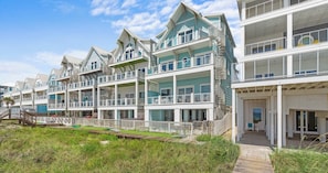 Un hotel frente al mar con varios balcones, una terraza de madera y cielo despejado.