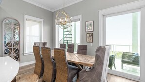 Un coin repas avec une table en bois et des chaises en osier, un lustre et un balcon agrémenté de mobilier d’extérieur.