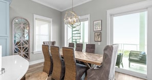 A dining area with a wooden table and wicker chairs, a chandelier, and a balcony with outdoor furniture. - Ocean-view Home 7BR Retreat (Panama City Beach)
