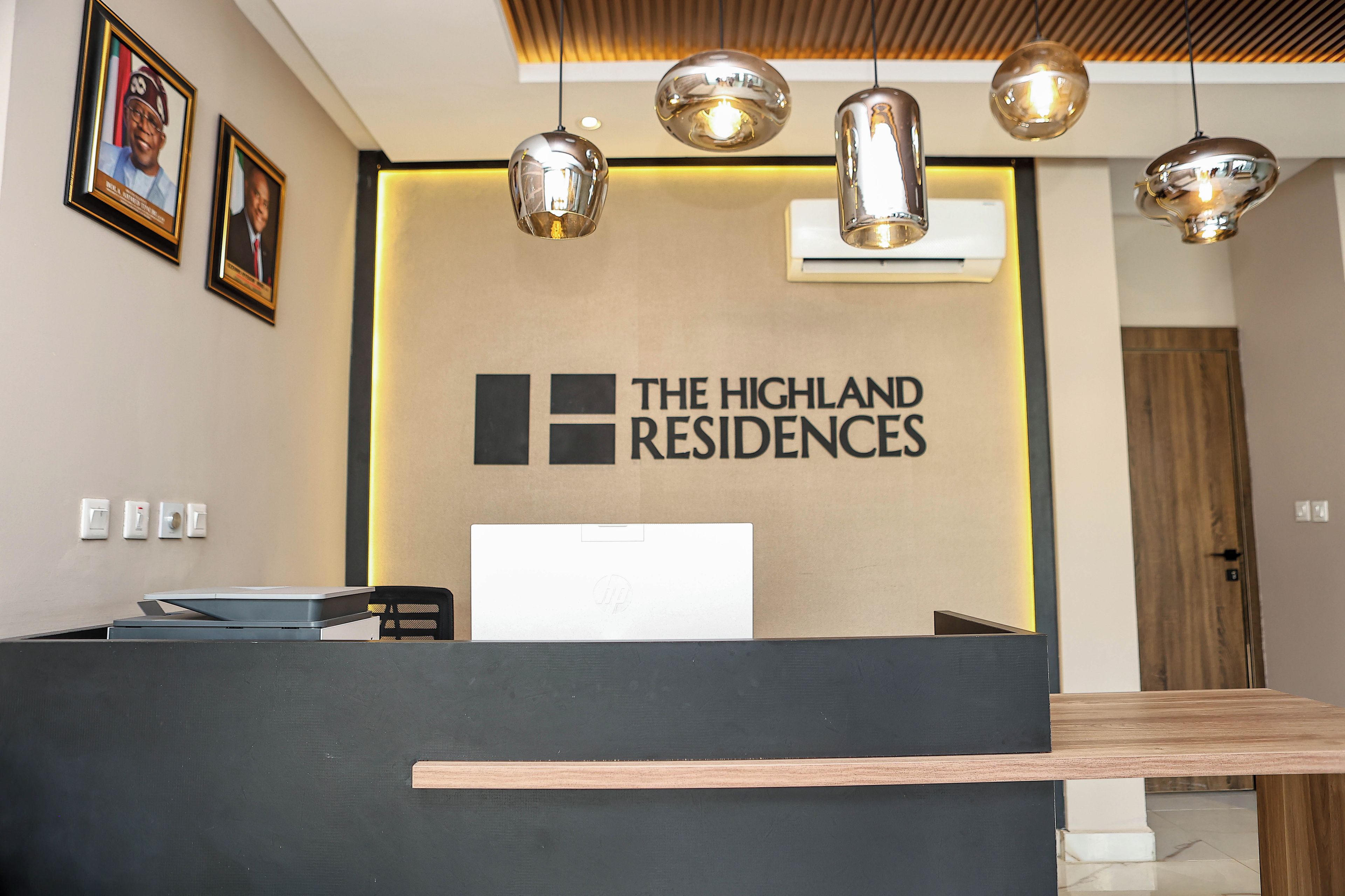Un comptoir d’accueil avec une pancarte indiquant « The Highland Residences » et un ordinateur portable posé dessus.
