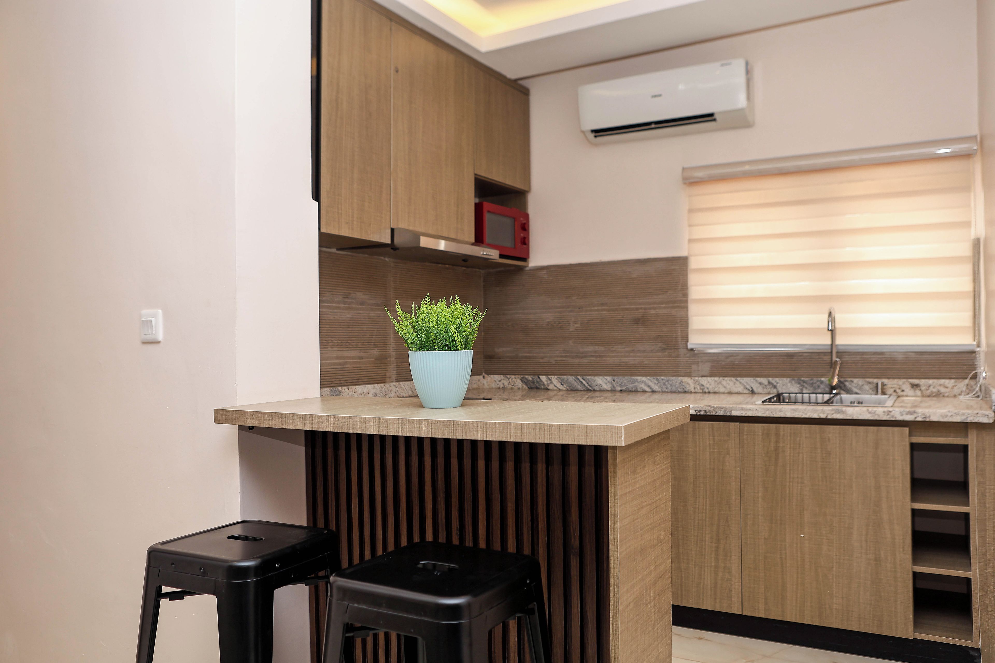 Una cocina moderna con armarios de madera, encimera de mármol, una pequeña planta en maceta y un taburete negro.