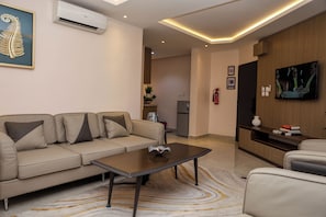 A modern living room with a sofa, coffee table, and a flat-screen TV mounted on the wall. - The Highland Residences (Abuja)