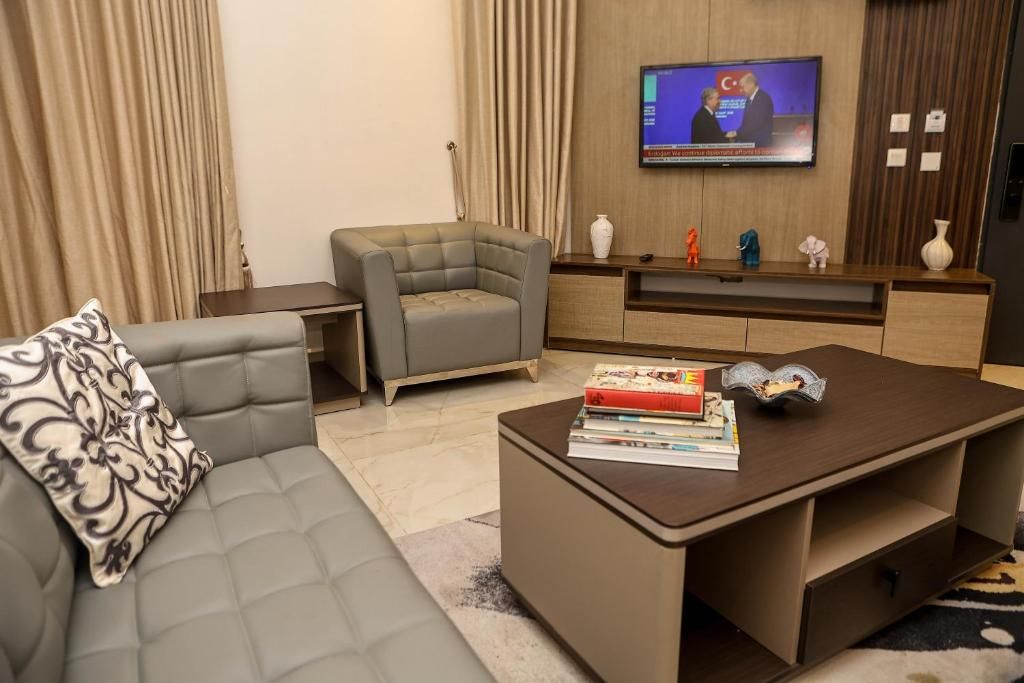 Una sala de estar moderna con un sofá gris, una mesa de centro con libros, un televisor montado en la pared y un mueble de entretenimiento de madera.