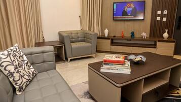 Una sala de estar moderna con un sofá gris, una mesa de centro con libros, un televisor montado en la pared y un mueble de entretenimiento de madera.