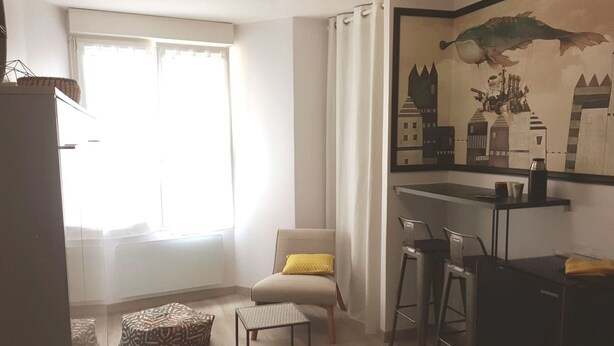 A modern living room with a sofa, a small table, a chair, a decorative wall piece, and a window with curtains. - Studio in the heart of downtown (Caen)