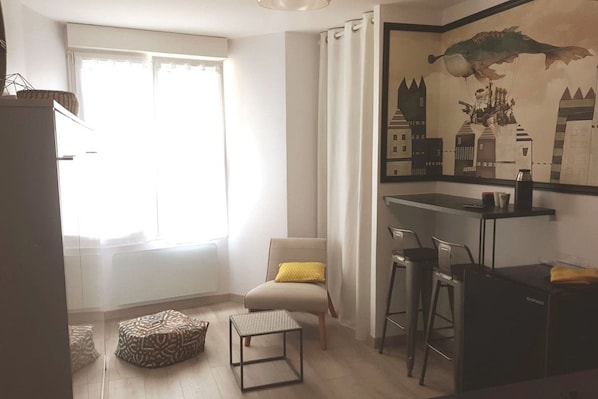 Een moderne woonkamer met een bank, een klein tafeltje, een stoel, een decoratief kunstwerk aan de muur en een raam met gordijnen.