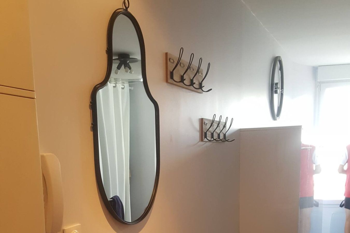 A room with a large oval mirror, a white cabinet, and wall-mounted hooks.