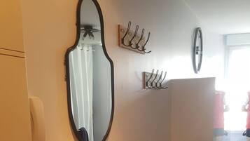 A room with a large oval mirror, a white cabinet, and wall-mounted hooks.