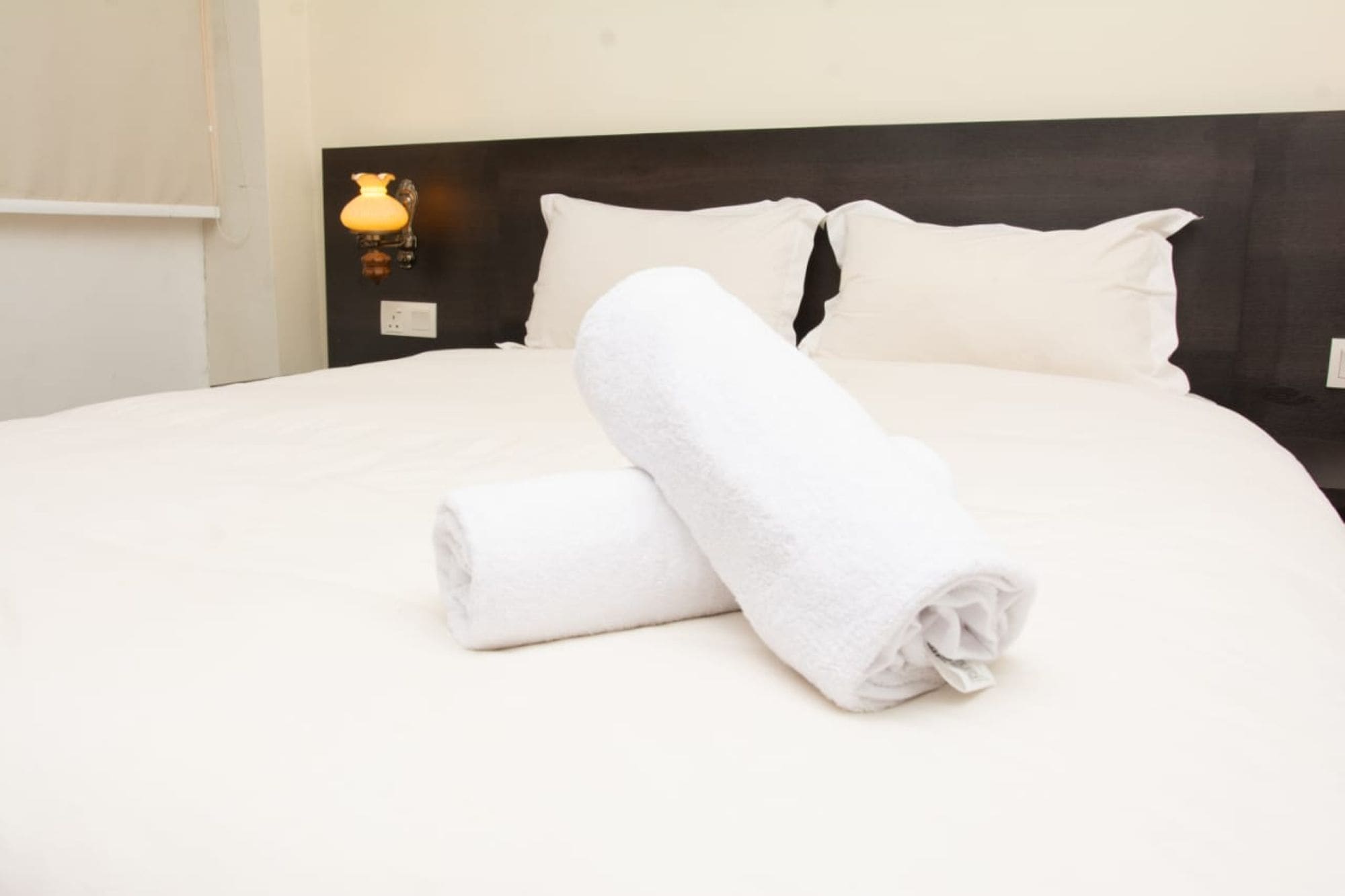 A neatly made bed with white linens and two rolled towels.